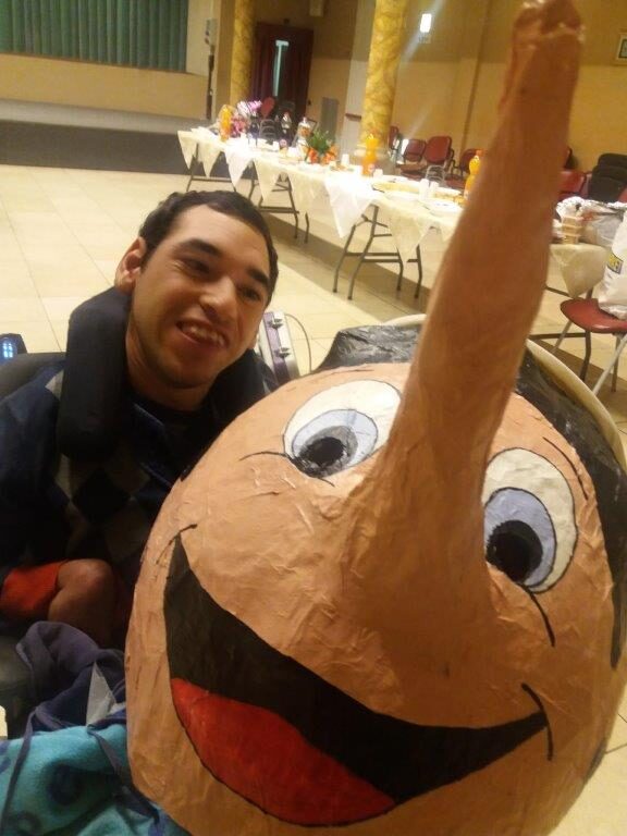 Lui, sorridente, accanto a una grande testa di Pinocchio in cartapesta, alla festa di Carnevale.