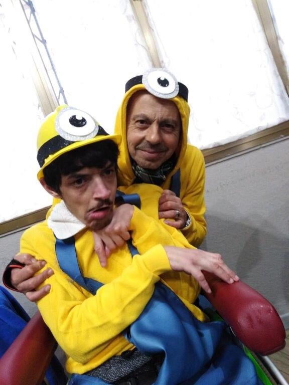 Un uomo vestito da Minion abbraccia un ragazzo in carrozzina, anche lui vestito da Minion.
