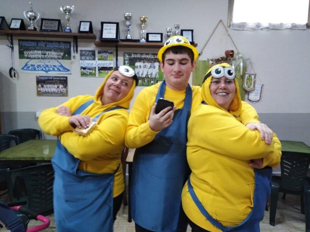 Tre amici vestiti da Minion in posa, uno con il telefono in mano.