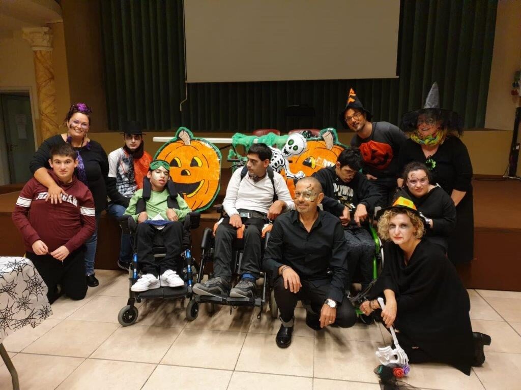 Ragazzi e volontari travestiti per Halloween, con zucche di cartone e cappelli da strega. Lui è seduto in prima fila, con la felpa verde.