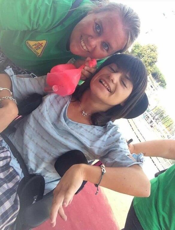 Una volontaria e una ragazza in carrozzina in un selfie all'aperto, sorridenti.